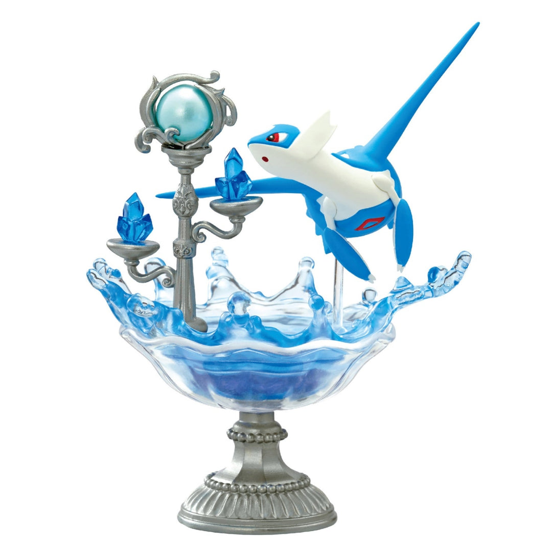 A decorative figure of Latios from Pokémon, shown flying above a splash of translucent blue resin inside a silver pedestal dish. A silver candelabra with blue crystal-like gems and a pearlescent blue orb stands beside it.