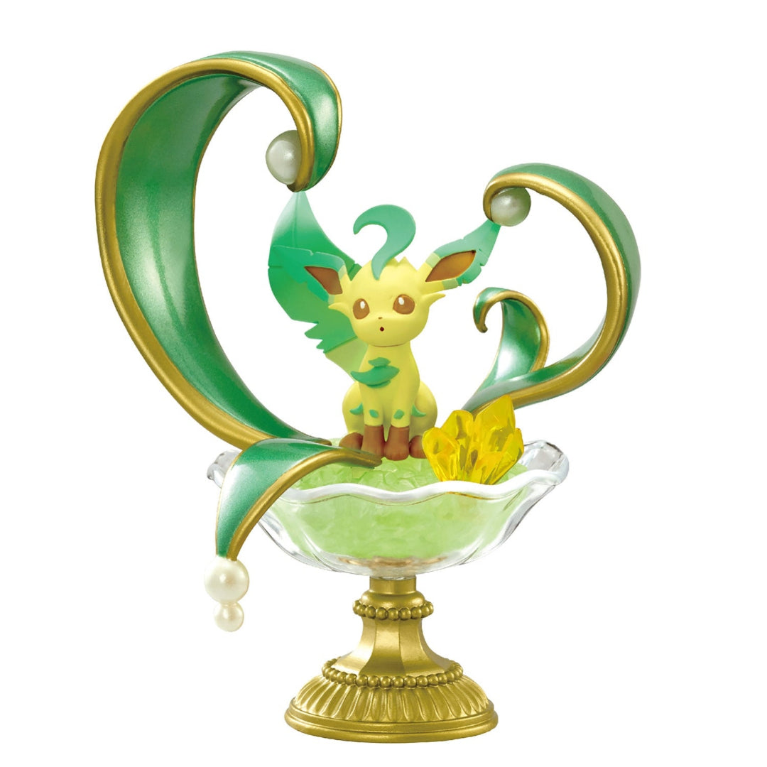 A decorative figure of Leafeon from Pokémon, sitting on a bed of translucent green crystals in a glass-like pedestal dish. Behind Leafeon are two large curling green and gold leaf-shaped structures with pearl-like accents, creating an elegant, nature-inspired design.