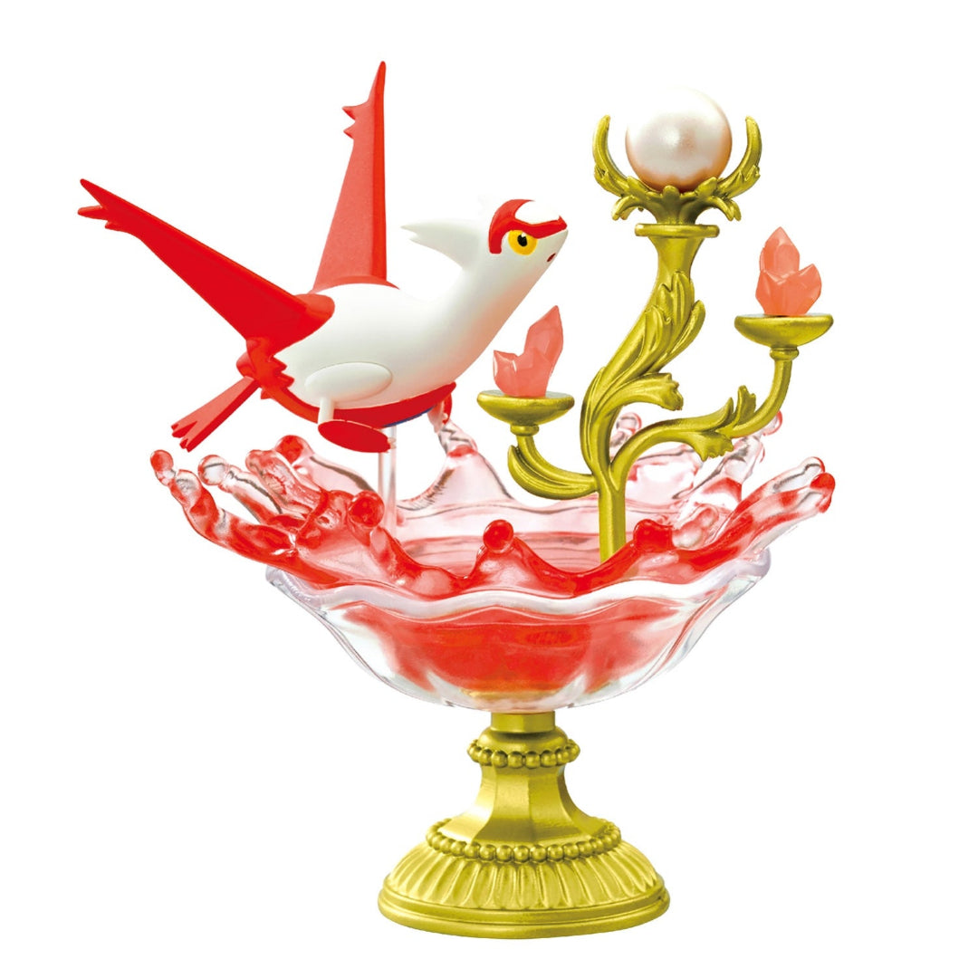 A decorative figure of Latias from Pokémon, shown flying above a splash of red translucent resin inside a gold-rimmed pedestal dish. To the right, a gold candelabra with crystal-like red gems and a pearl-like orb adds an ornate touch.