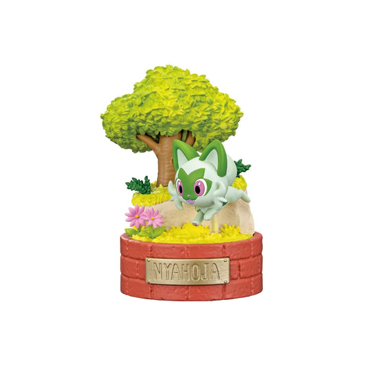A small Pokémon figure of Nyahoja (Sprigatito) leaping above yellow flowers on a round red brick-style base labeled “NYAHOJA.” The scene includes a lush green tree and pink flowers, creating a cheerful forest setting.